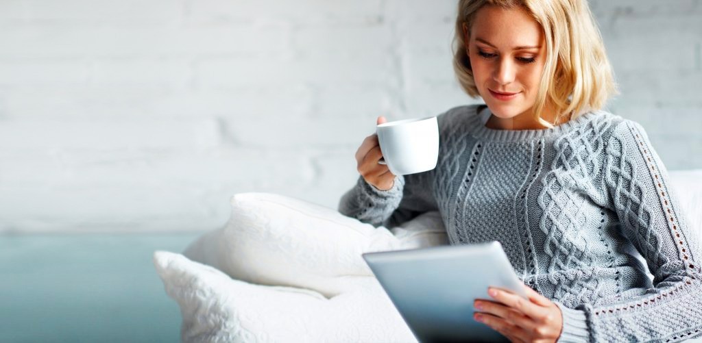 Woman on couch with tablet and coffee mug.